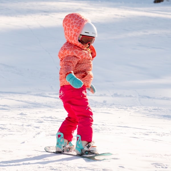 person in grey pants and orange jacket looking down at their skiis