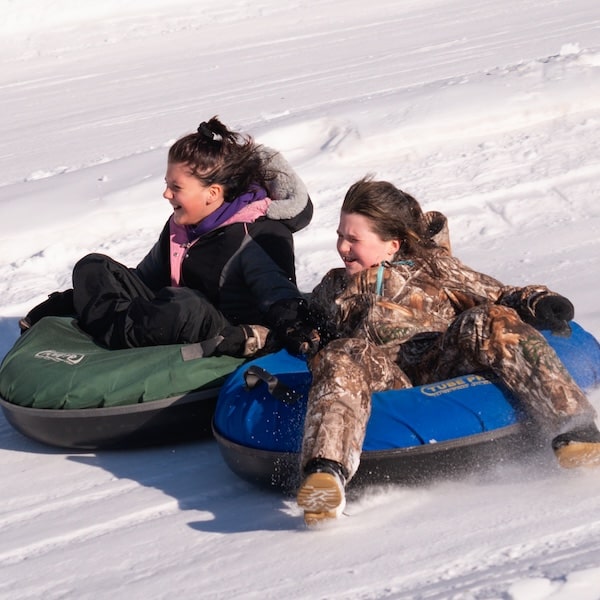 Two young women in sledding tubes sliding down a hill, fast.